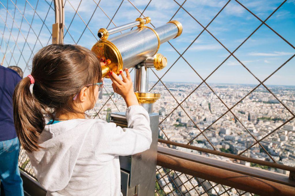 Girl looking through a telescope on top of the eiffel tower