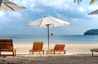 Two beach chairs under a white umbrella on the beach facing the ocean