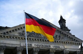 A German flag blowing in front of a building featuring German text
