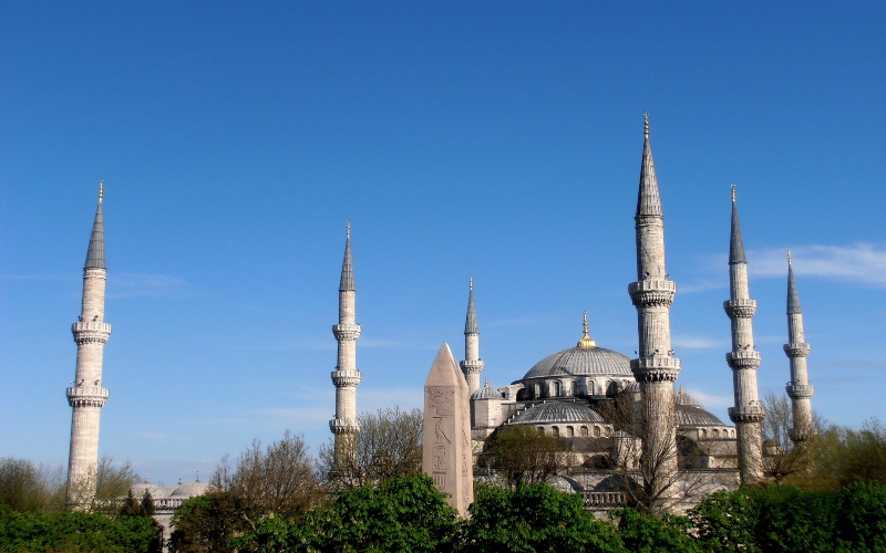 a picture of the blue mosque that includes all six pillars the sky is blue and there is surrounding foliage