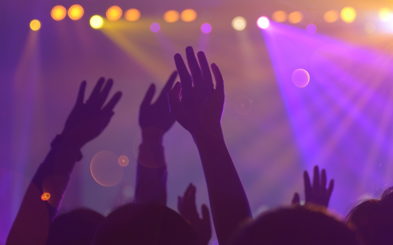 Slightly blurred image of people's arms in the air at a concert with bright lights in the background