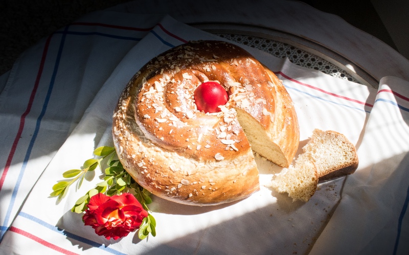 a picture of greek bread with a red egg in the middle covered in sunlight on a cloth with a flower