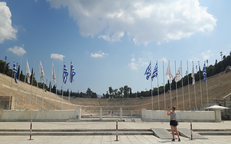 a view of the curved panathenaic stadium with a woman on the right and flags on each side of the stadium