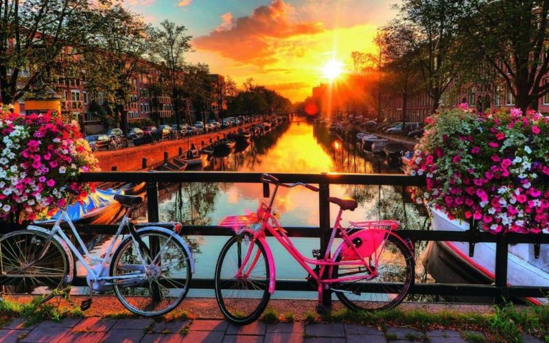 Brightly colored bikes on a bridge over a canal in Amsterdam at sunset.
