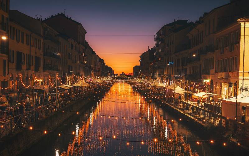 A river in Milan with fairy lights hanging over it at sunset.